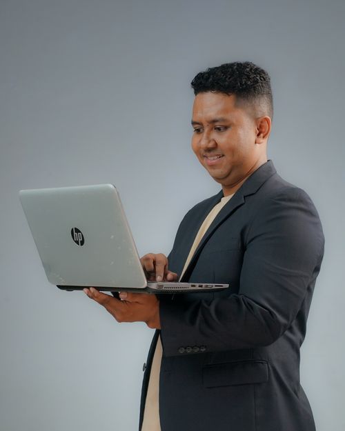 Free Confident young man in a suit working on a laptop in a studio setting. Stock Photo