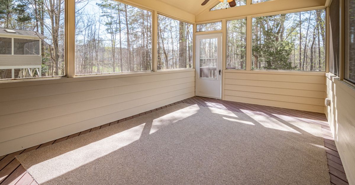 Spacious sunroom featuring glass panels and a ceiling fan, offering scenic woodland views.