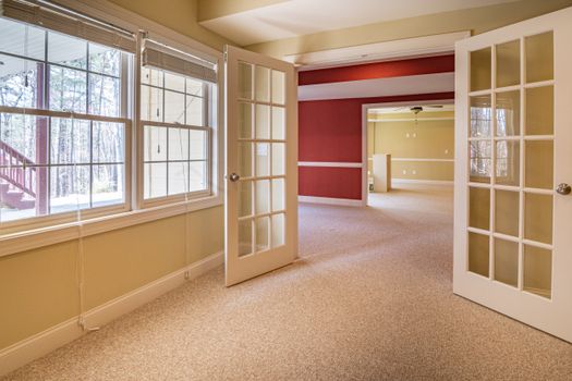 Bright and spacious empty room featuring French doors, large windows, and a warm color palette.