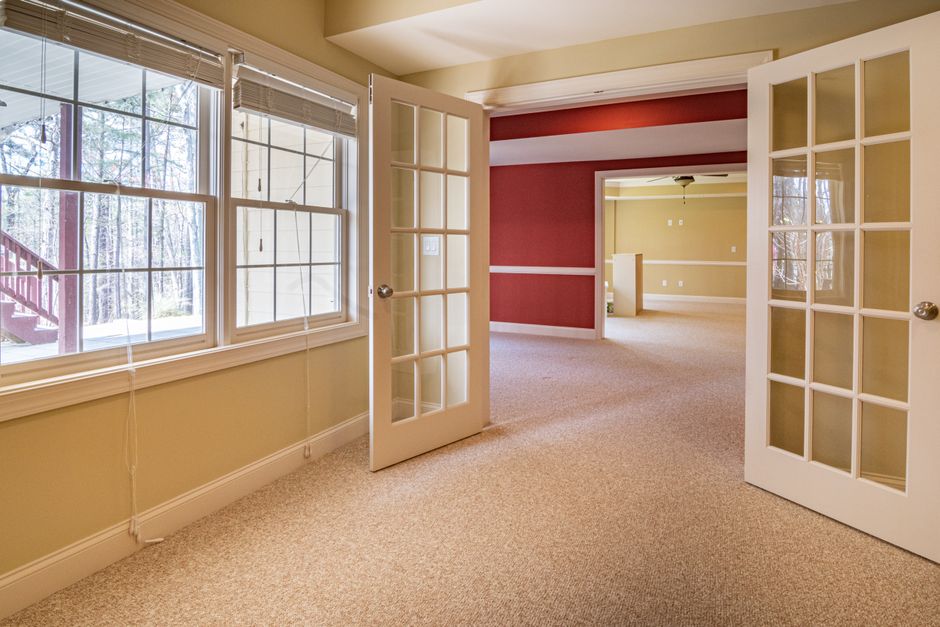 Bright and spacious empty room featuring French doors, large windows, and a warm color palette.