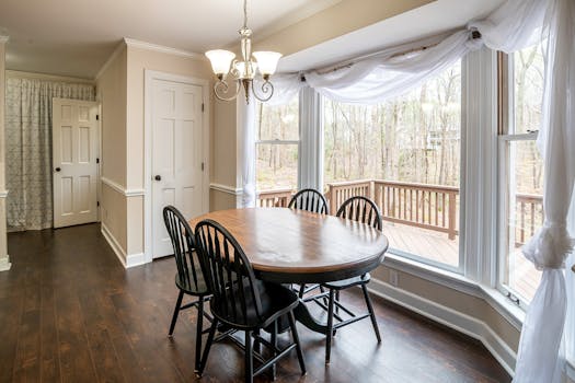 Bright dining area with large windows, wooden table, and chairs overlooking a deck.