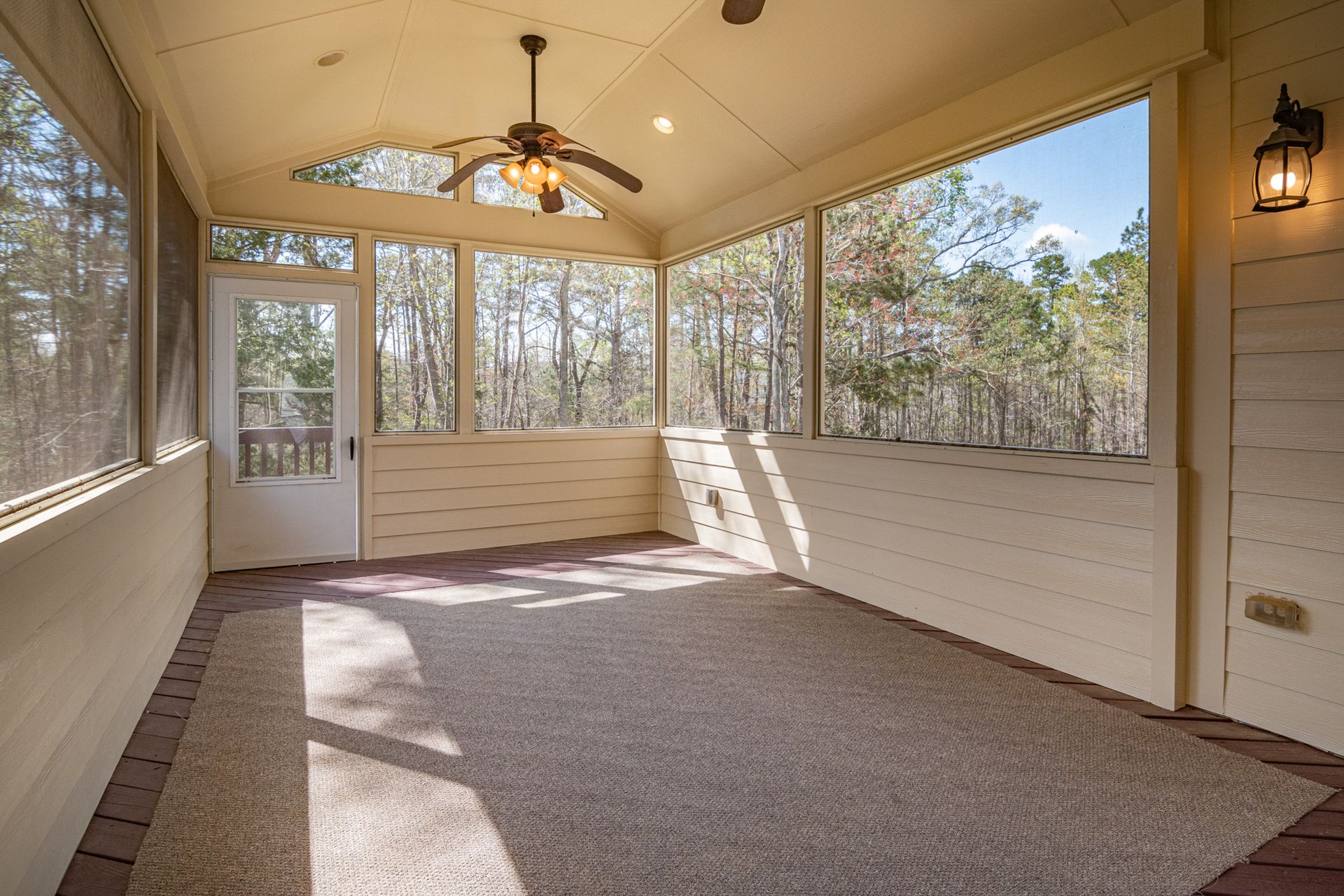 Bright empty porch with ceiling fan and large glass windows revealing a forest view.