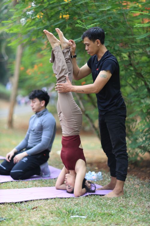 Free Yoga instructor assisting a headstand pose in a Jakarta park. Stock Photo