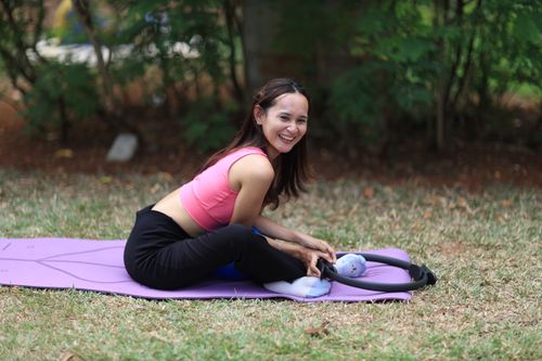 Free A woman smiling while doing yoga on a purple mat in a park in Jakarta, Indonesia. Stock Photo