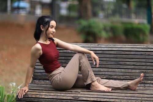 Free Young woman relaxing on a wooden bench in Jakarta park during the day. Stock Photo