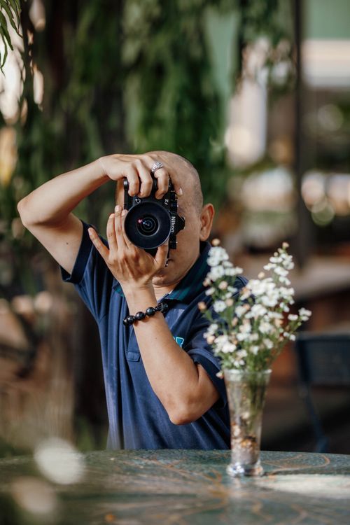 Free A photographer focuses through his camera on indoor floral arrangements. Stock Photo