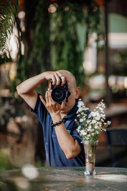 Free Portrait of a photographer capturing nature indoors, with floral foreground. Stock Photo