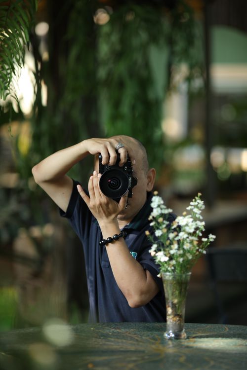 Free Man taking photo in botanical indoor setting with greenery. Stock Photo