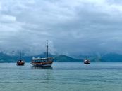 Picturesque view of vessels with wooden masts sailing on sea with rippled water behind mounts under sky with low clouds in overcast weather in afternoon