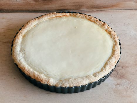 A freshly baked cheesecake tart with a golden crust sits elegantly on a rustic wooden surface, enticing and mouthwatering.