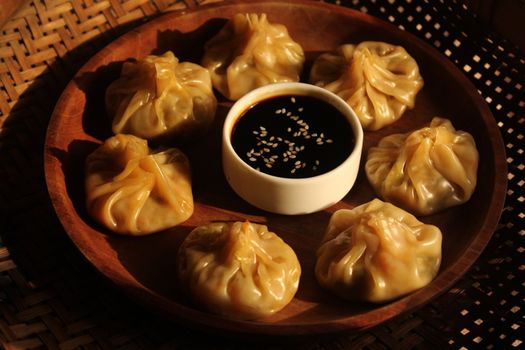 Wooden bowl of steamed dumplings with soy sauce dip, perfect for an Asian cuisine theme.