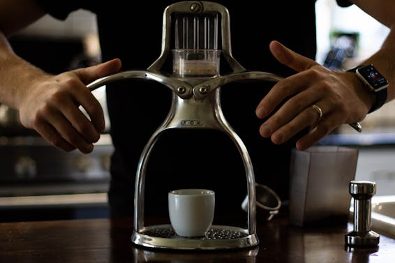Crop anonymous slim male in wristwatch and golden ring using stainless steel manual drip coffee machine with ceramic cup while preparing hot drink at home
