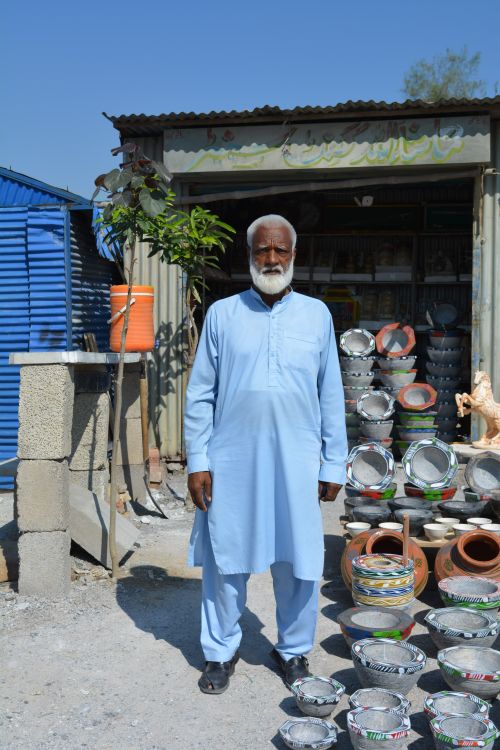 Free A Pakistani artisan in traditional attire stands outside a craft shop displaying handmade pots and vessels. Stock Photo