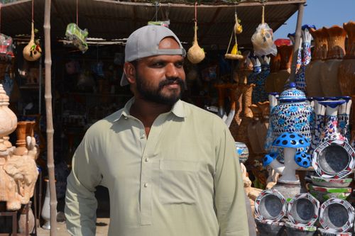 Free A young man stands in front of a Pakistani handicraft shop displaying colorful pottery and sculptures. Stock Photo