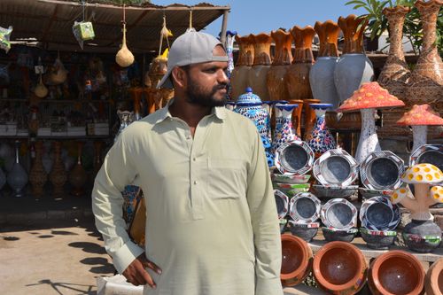 Free Man in traditional attire at a vibrant outdoor artisan pottery market in Pakistan. Stock Photo
