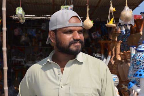 Free Pakistani artisan standing in a vibrant craft market displaying traditional pottery. Stock Photo
