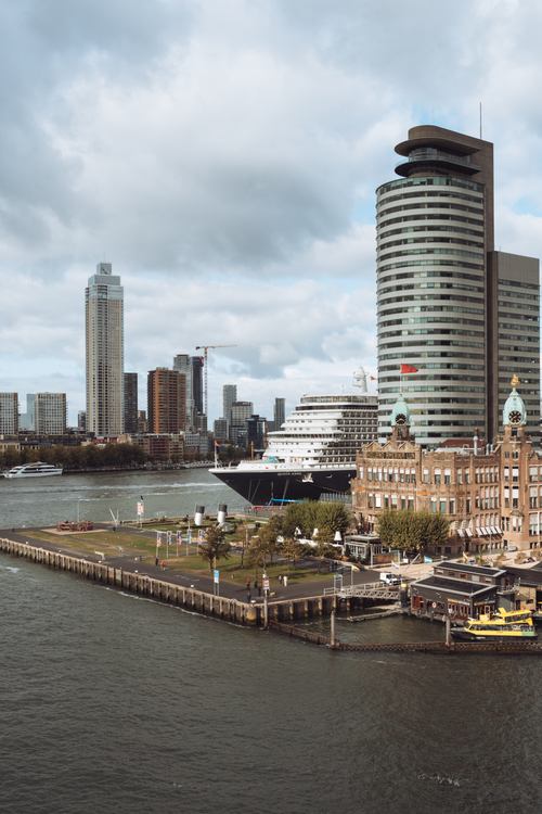 Free A scenic view of Rotterdam's modern skyline featuring a cruise ship docked at the harbor. Stock Photo