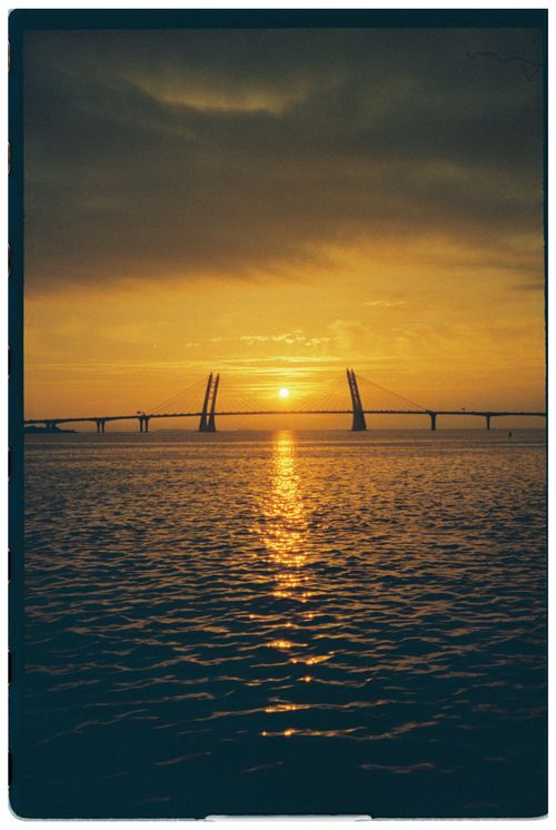 Free A breathtaking sunset over a bridge, casting golden reflections on the water. Stock Photo