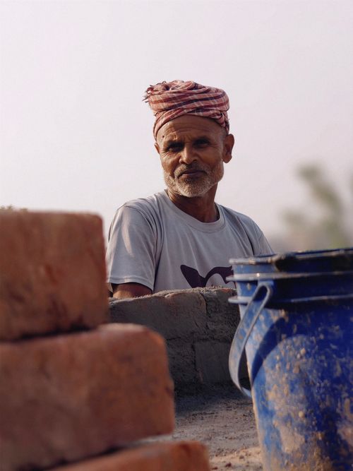 Free Elderly man in turban working with bricks and bucket outdoors, depicting labor and resilience. Stock Photo