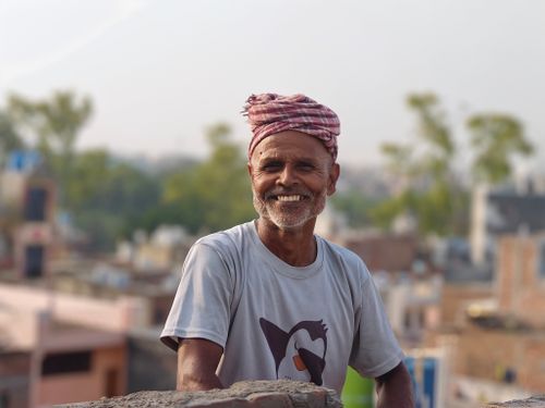 Free A cheerful elderly man wearing a pink turban and t-shirt stands outside, smiling with an urban background. Stock Photo