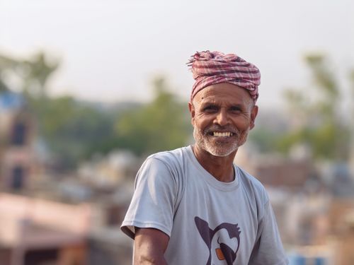 Free Elderly man in a casual shirt smiling during the day outdoors with a blurred nature background. Stock Photo