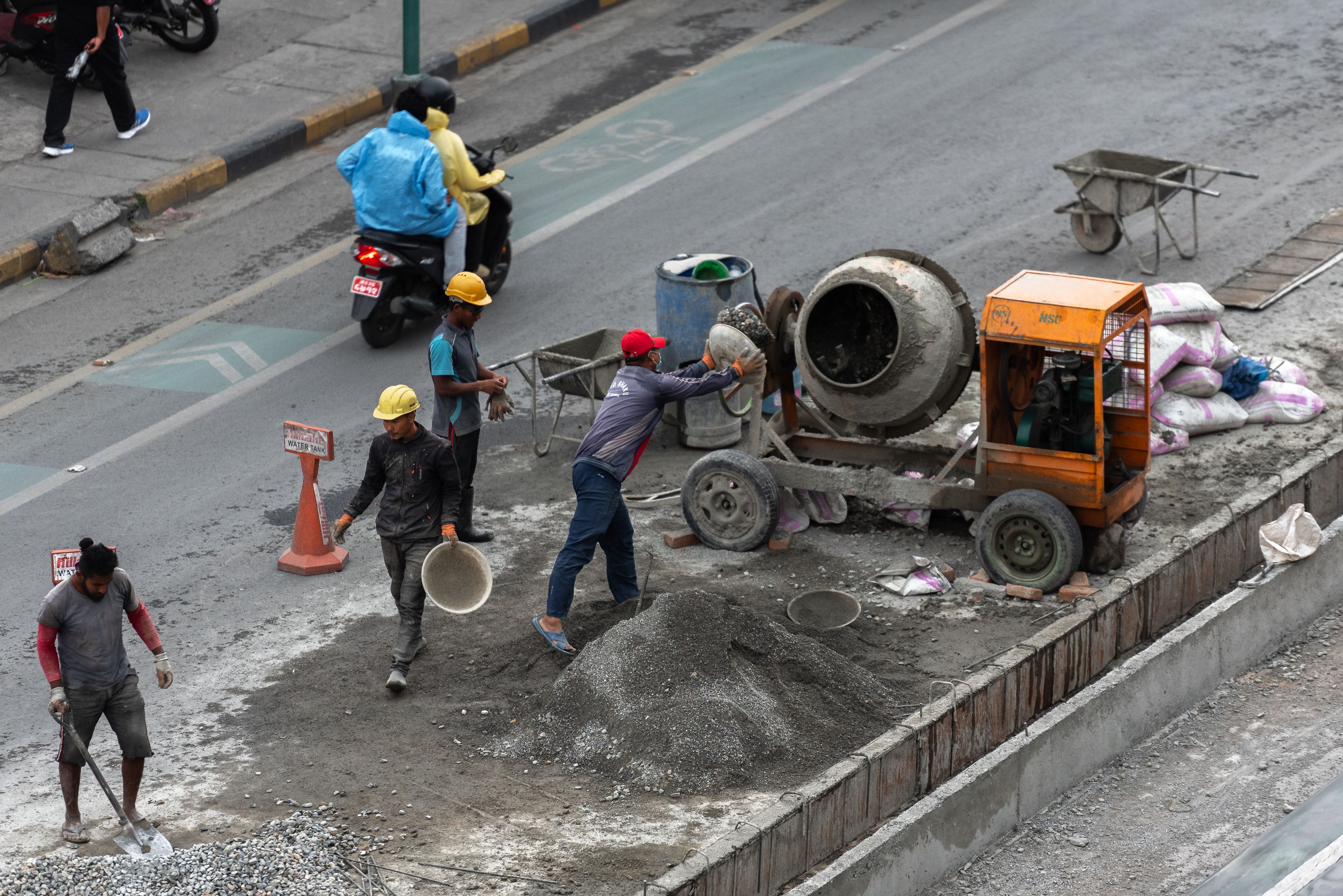 Construction workers mixing concrete on a street in Pokhara, Nepal, showcasing urban development.