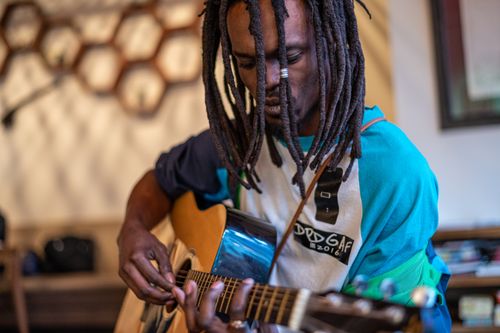 Free Crop concentrated young casual African American male musician with dreadlocks playing acoustic guitar in modern cafe Stock Photo