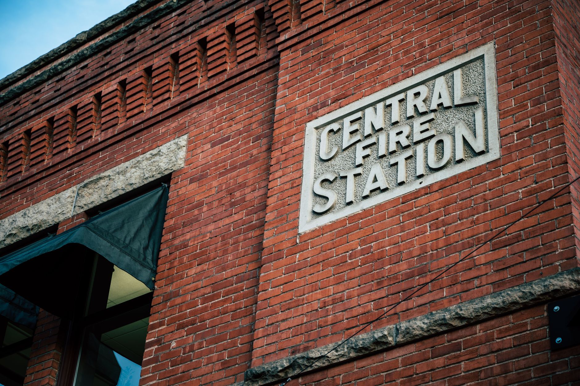 From below of red brick wall of aged building with central fire station inscription on signboard against blue sky