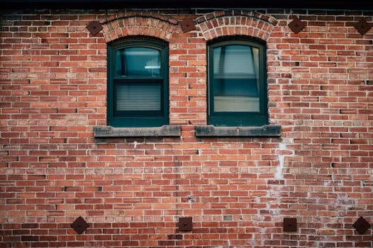 A rustic brick facade featuring two arched windows with green frames, showcasing vintage architecture.