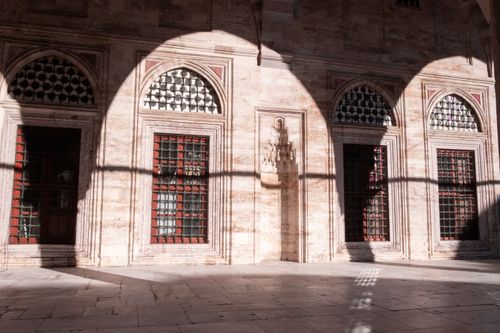 Free Scenic view of arched shadows falling on an ancient Istanbul wall with red-paneled windows in sunlight. Stock Photo