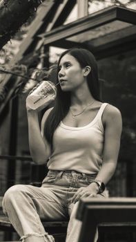 一位穿着休闲装的年轻少数族裔女性，自信地坐在长凳上，从低角度看去，正用吸管喝着新鲜的冰沙