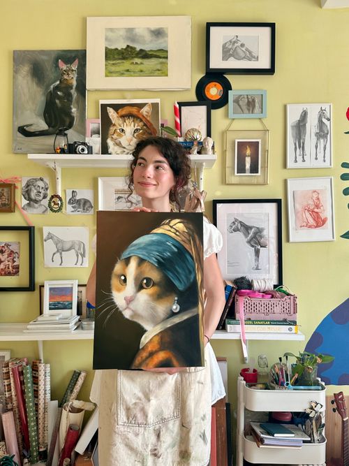 Free A young female artist proudly displays her humorous cat painting in a colorful and creative studio. Stock Photo