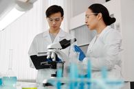 亚洲科学家穿着实验室外套，在实验室环境中用显微镜讨论研究