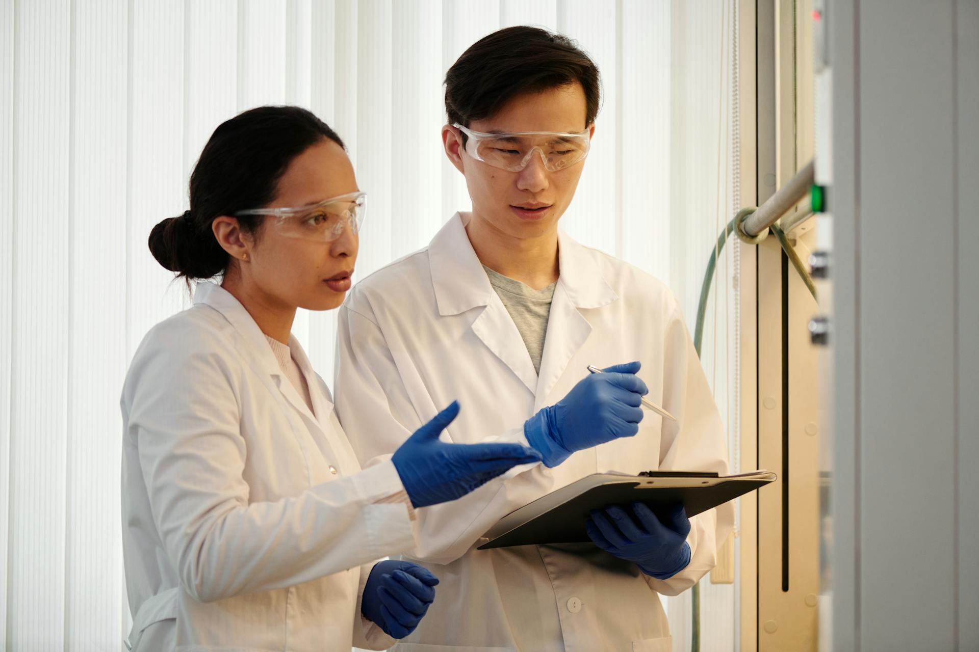 Researchers discussing data in a laboratory setting, wearing safety gear and blue gloves.