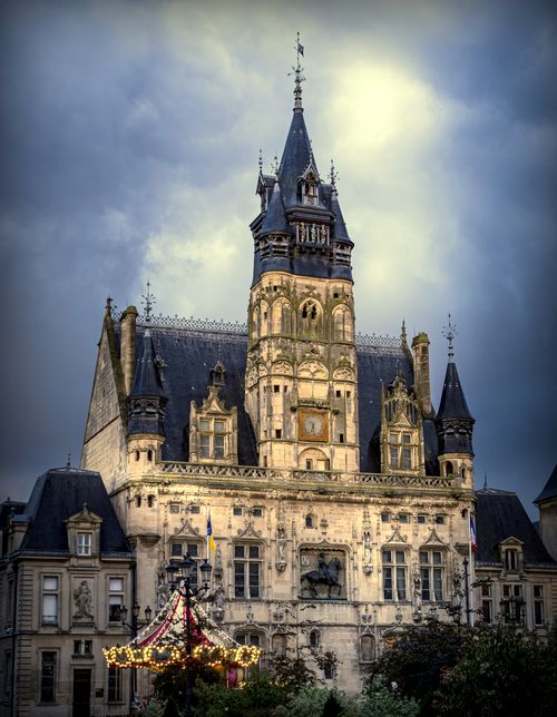 Free Gothic-style town hall building under a dramatic cloudy sky with decorative architectural details. Stock Photo