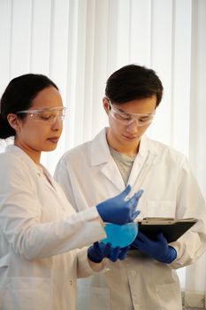 两名穿着实验服的科学家正在讨论关于蓝色液体的实验