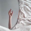 Round mirror on white towel with hand reflection of crop anonymous female with long nails in light room