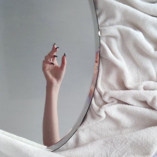 Free Round mirror on white towel with hand reflection of crop anonymous female with long nails in light room Stock Photo
