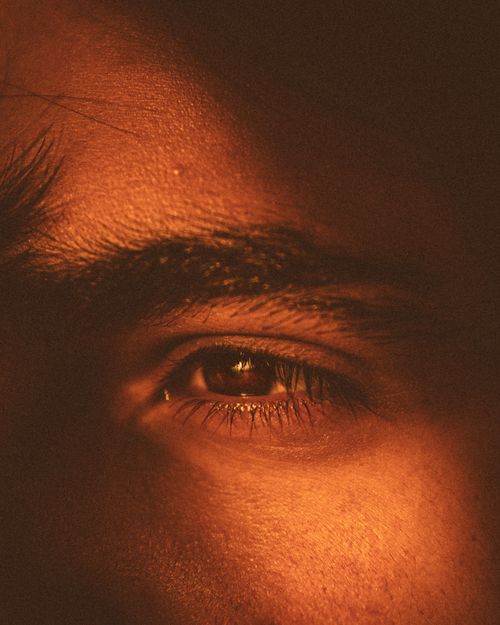 Free A close-up of an eye highlighted with warm, dramatic lighting creating an intense artistic effect. Stock Photo