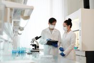 两名科学家在实验室里戴着口罩，用显微镜讨论研究