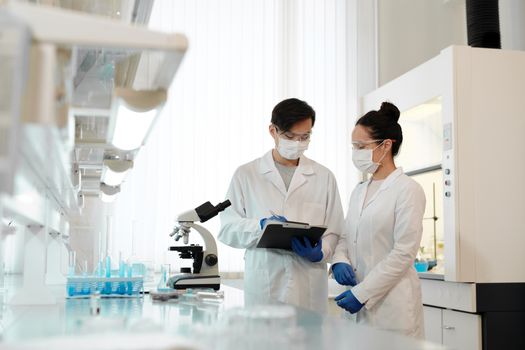 两名科学家在实验室里戴着口罩，用显微镜讨论研究