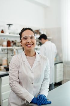 一位自信的女科学家穿着实验室外套，在室内实验室环境中微笑着工作