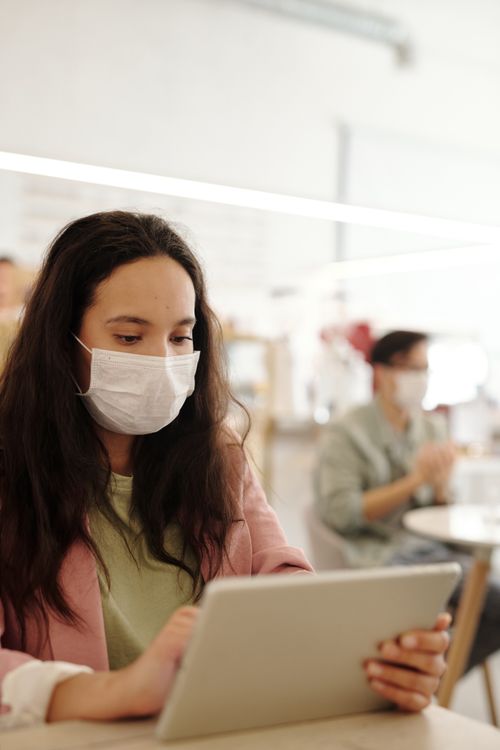 Free Woman wearing face mask using tablet in a cafe setting, focused and attentive. Stock Photo