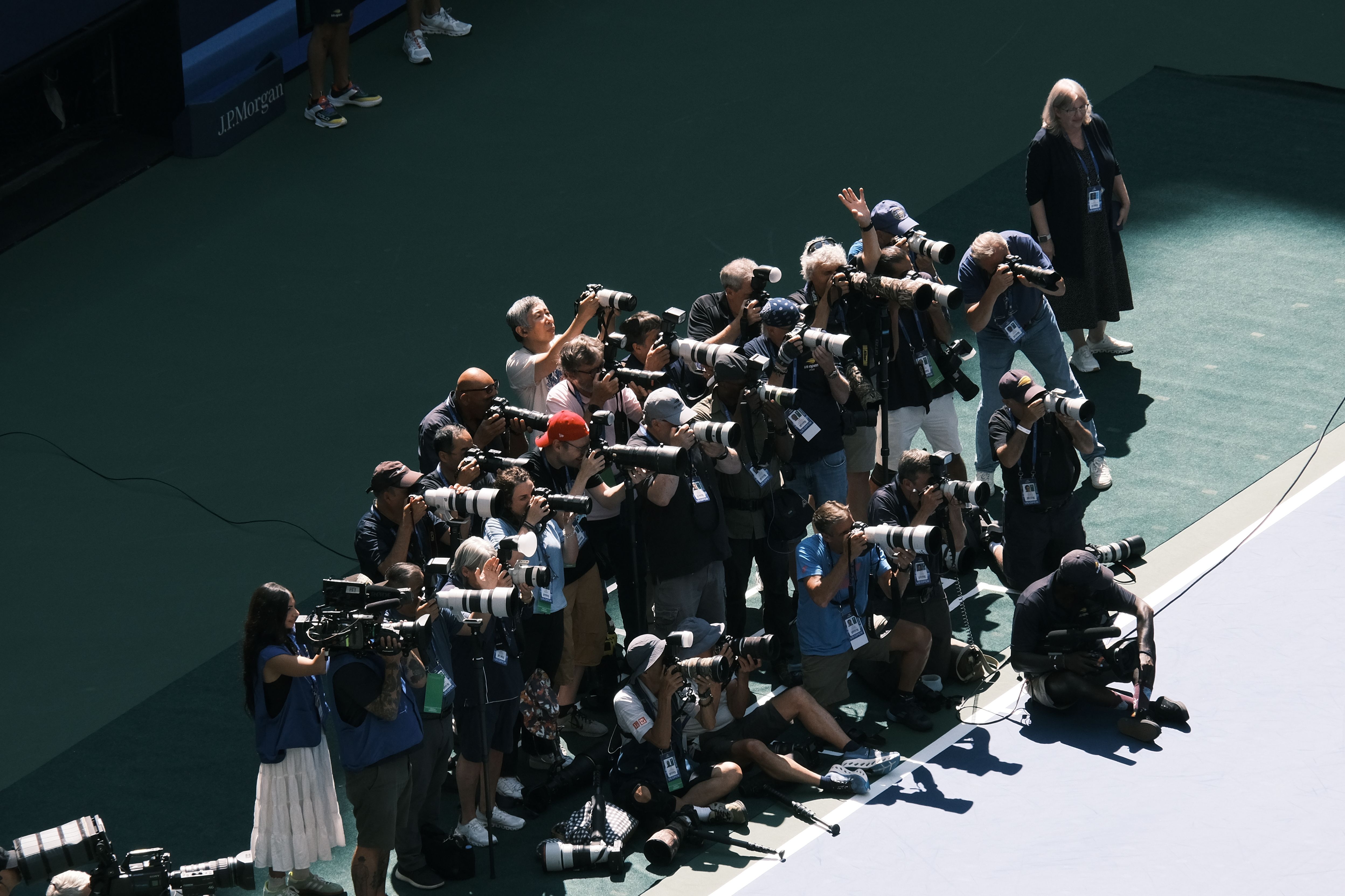 屋外イベントで、カメラとレンズを持った大勢の写真家たちが写真を撮っている。