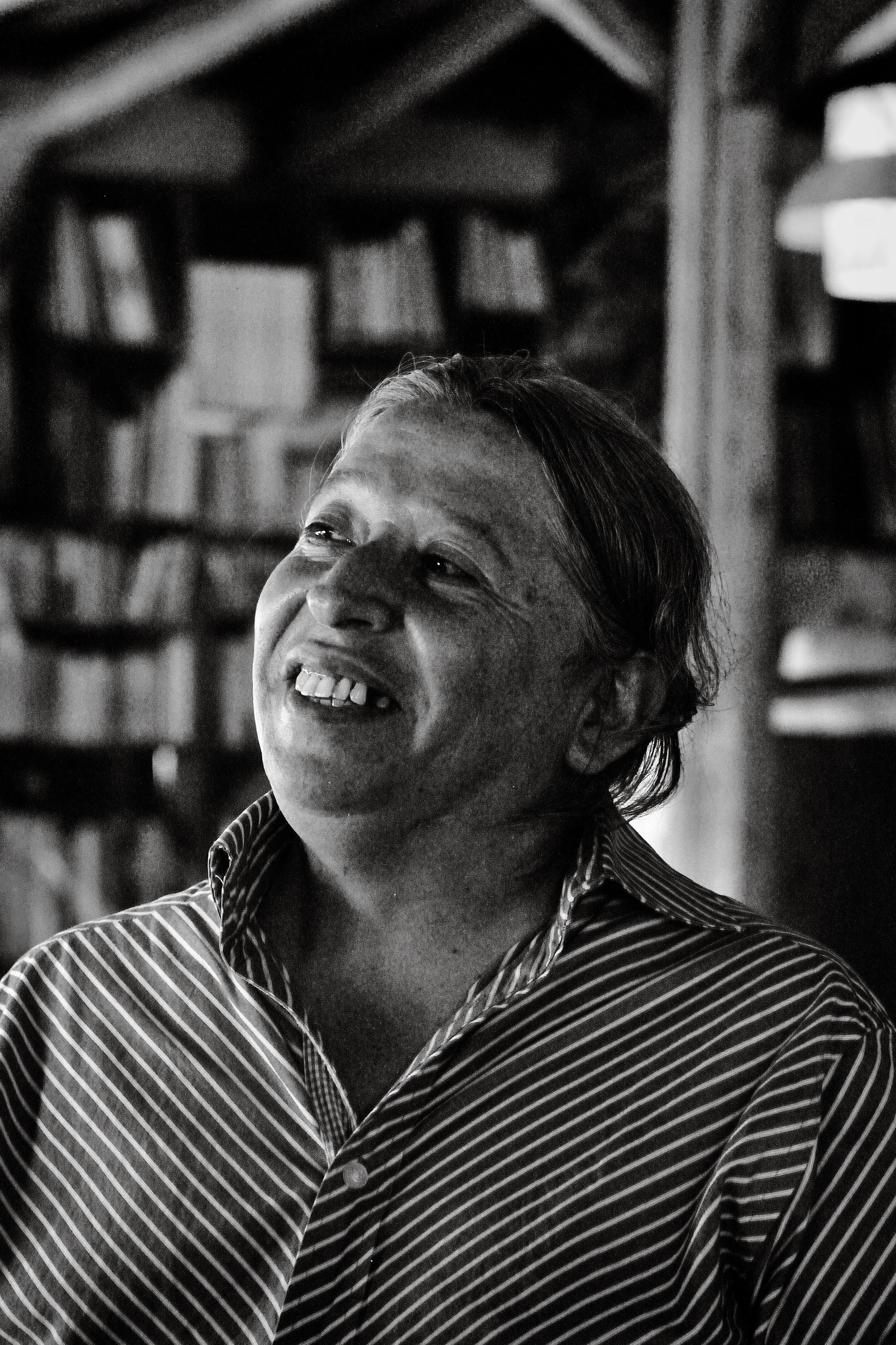 Fotomural Retrato emotivo en blanco y negro de un adulto sonriendo en el interior de un edificio, con una biblioteca de fondo.