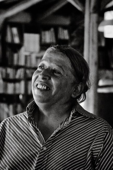 Fotomural Retrato emotivo en blanco y negro de un adulto sonriendo en el interior de un edificio, con una biblioteca de fondo.