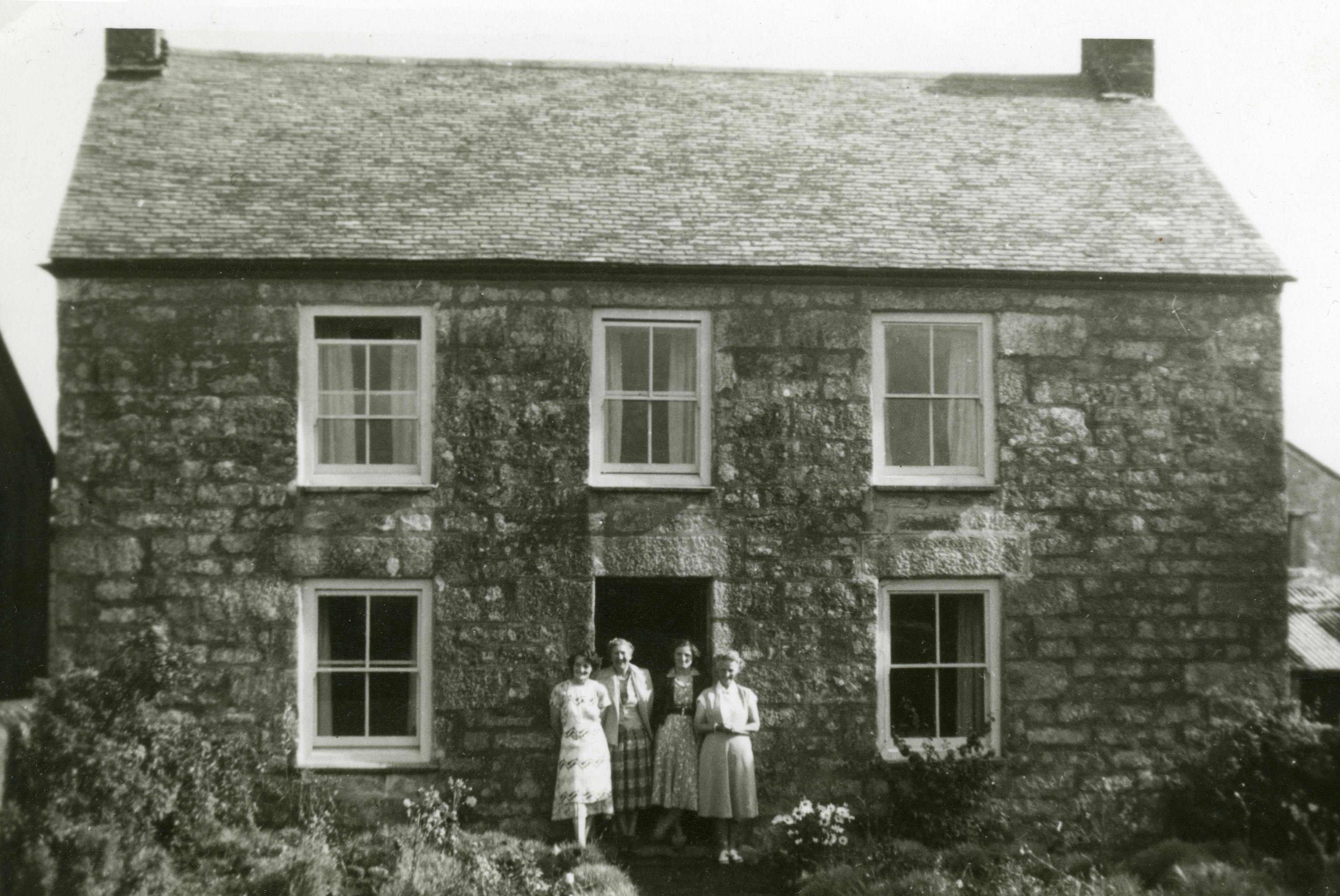 Grayscale Photo of Four Women Standing in Front of House