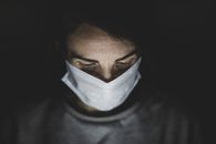 在黑暗环境中，一个戴着口罩、沉思的人被拍摄下来，营造出喜怒无常的氛围