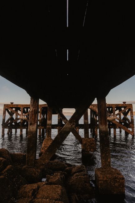 Explore a striking perspective beneath a rustic wooden pier over water in West Kilbride, Scotland.