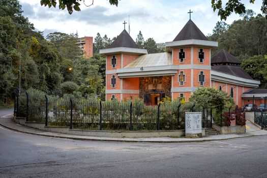 A picturesque Venezuelan church with a brick facade, lush greenery, and a scenic backdrop.